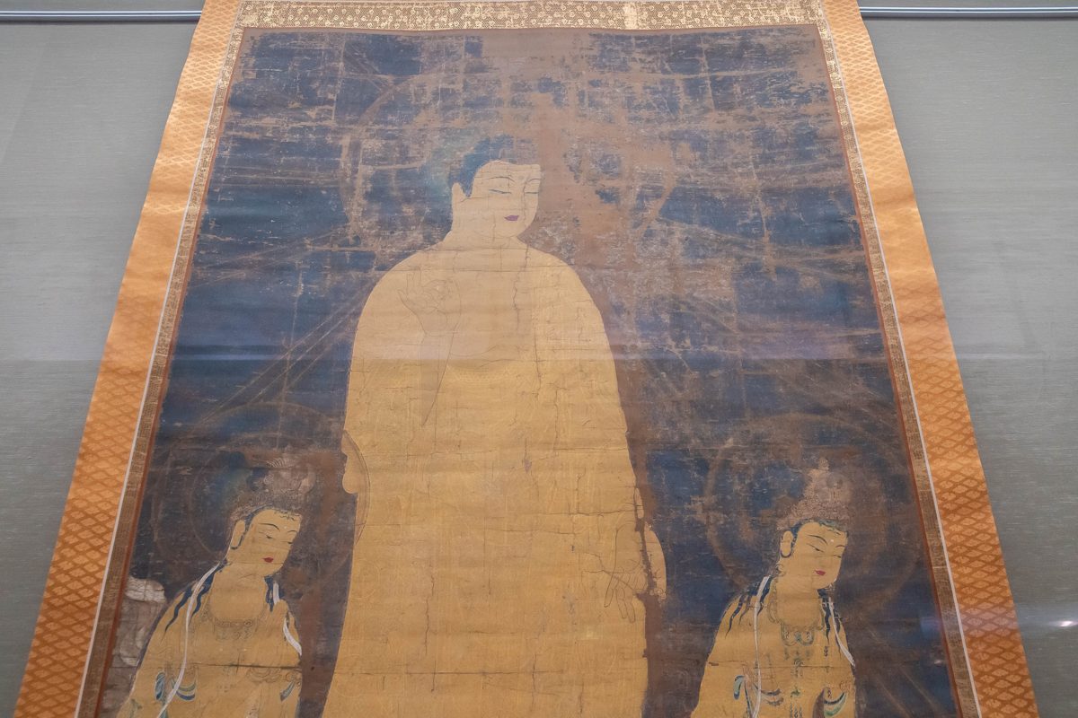 A large hanging scroll painting of a seated figure in a museum display case