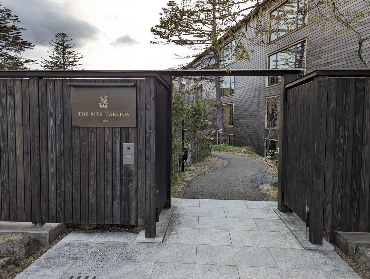 A dark wooden gate with a bronze sign reading The Ritz-Carlton Nikko, and a path leading to the hotel