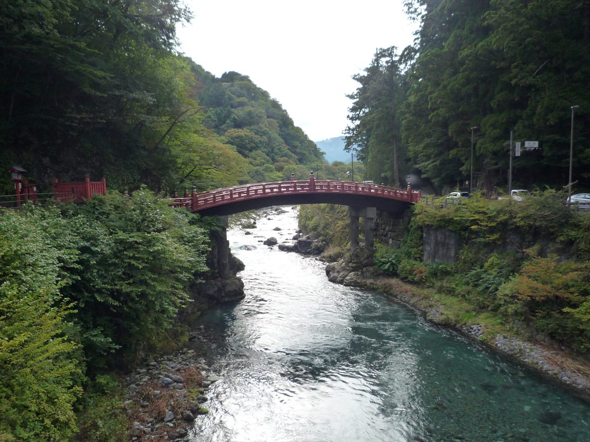 A red arched bridge over a clear river between forested banks