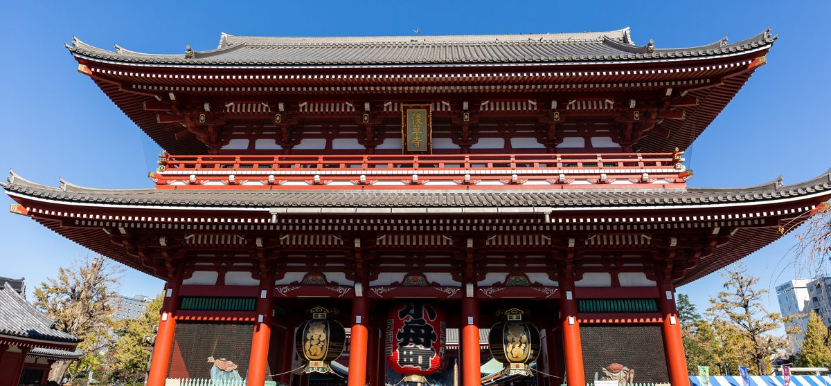 The red two-story Hozomon gate of Senso-ji with large lanterns under a clear blue sky