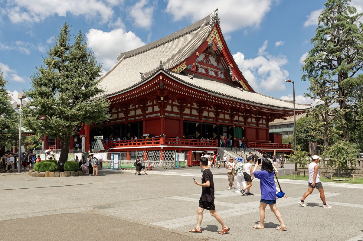 The main hall of Senso-ji with a sweeping tiled roof, pine trees and a wide stone courtyard