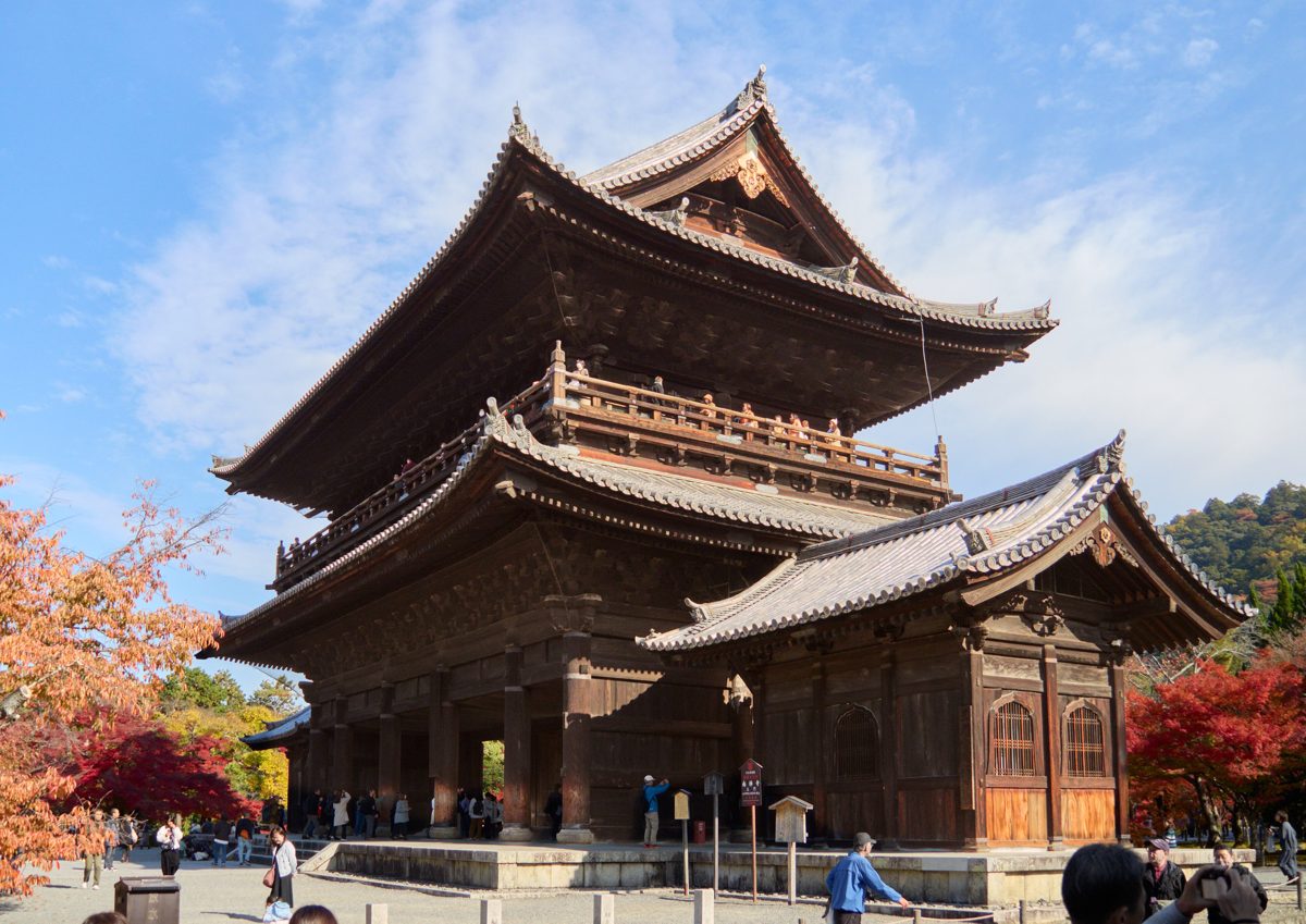 The massive wooden Sanmon gate of Nanzenji with red autumn maples under a blue sky