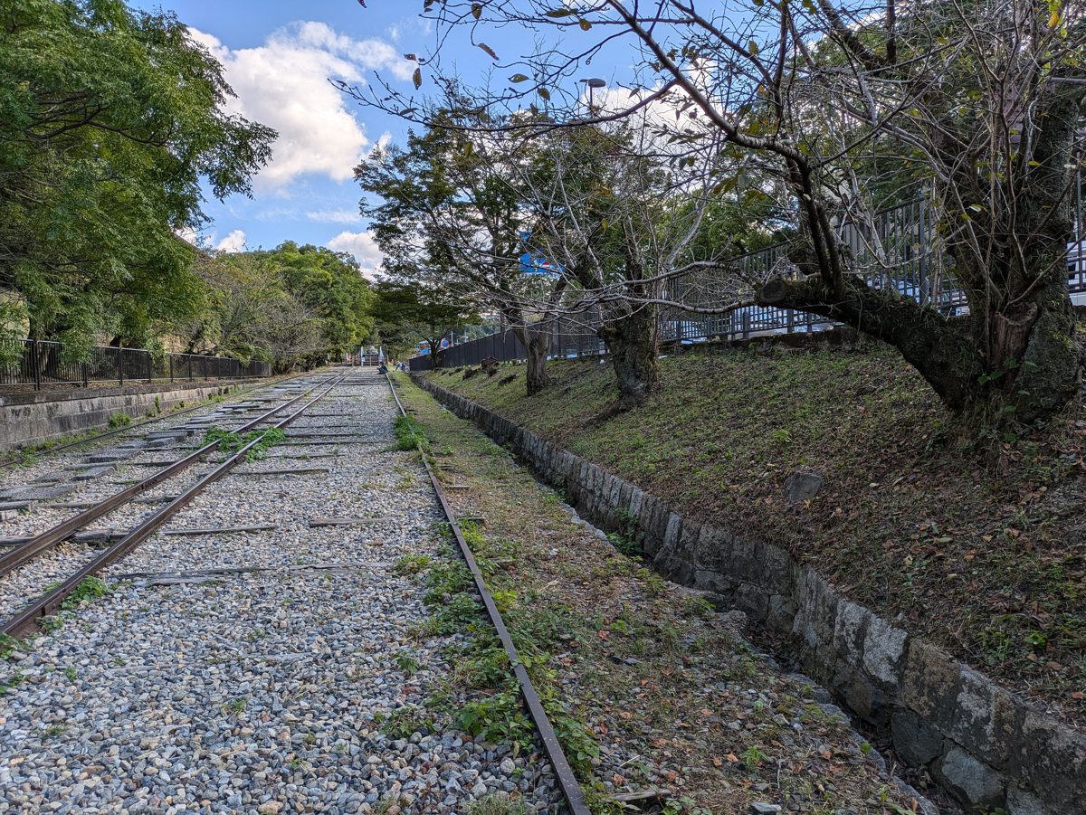The old rails of the Keage Incline running between trees under a partly cloudy sky