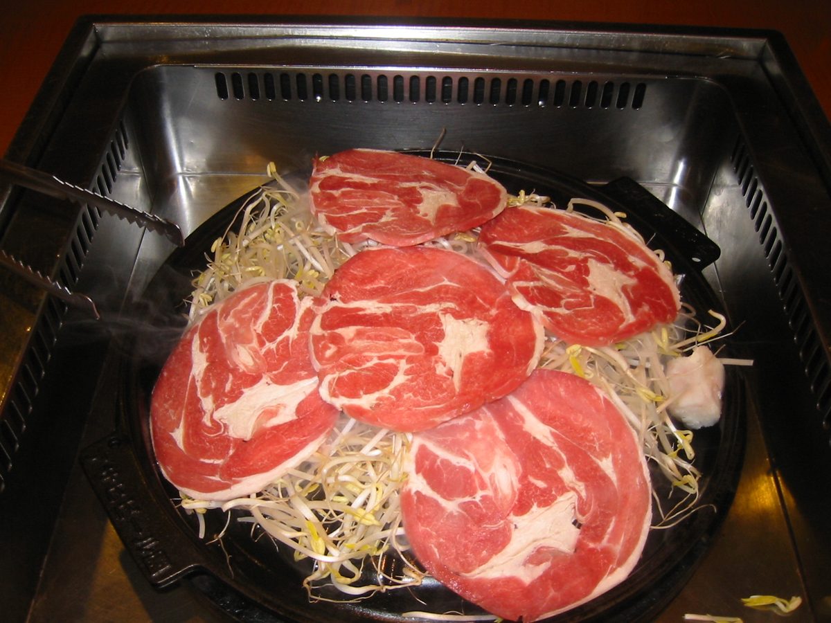 Slices of raw lamb on a domed grill over bean sprouts