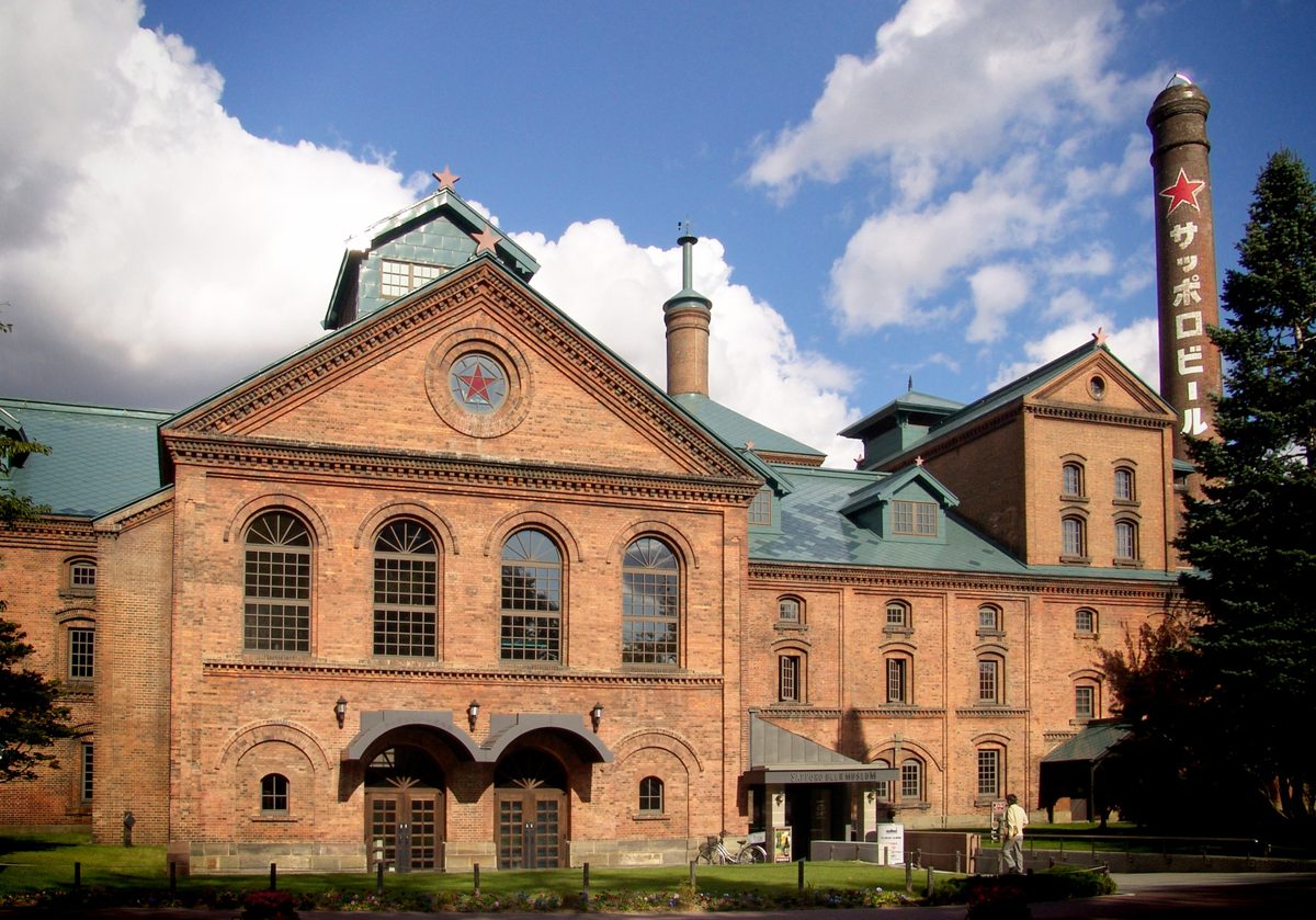 A red-brick building with arched windows and a tall chimney under a blue sky