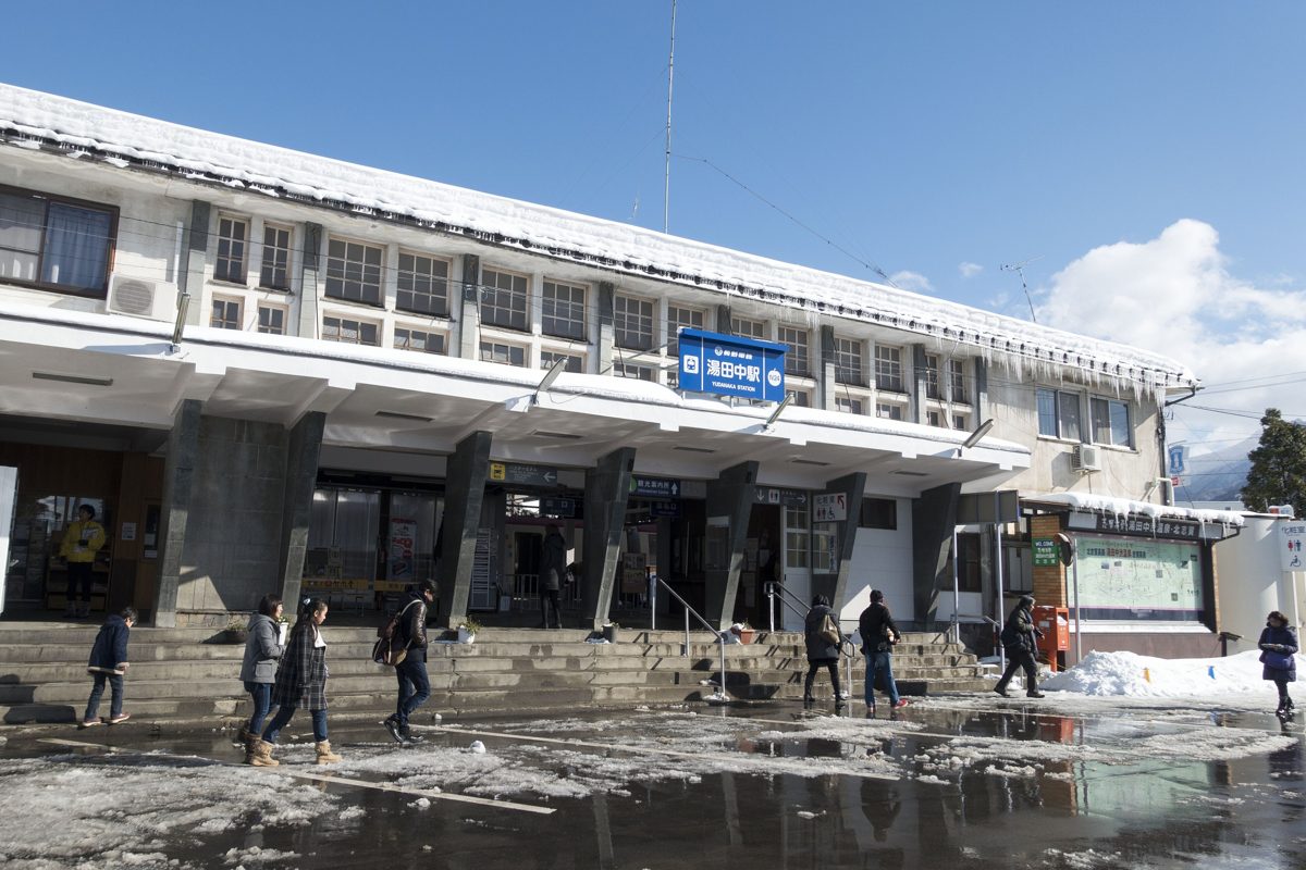 The front of Yudanaka Station in winter with patches of snow and a few people walking
