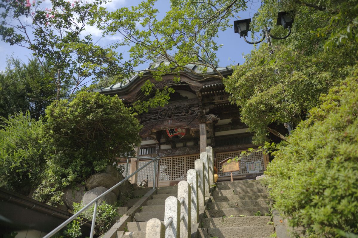 Stone steps leading up to a carved wooden shrine among green trees