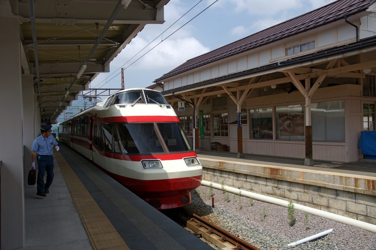A red and white train standing at a platform under a wooden canopy at Yudanaka Station