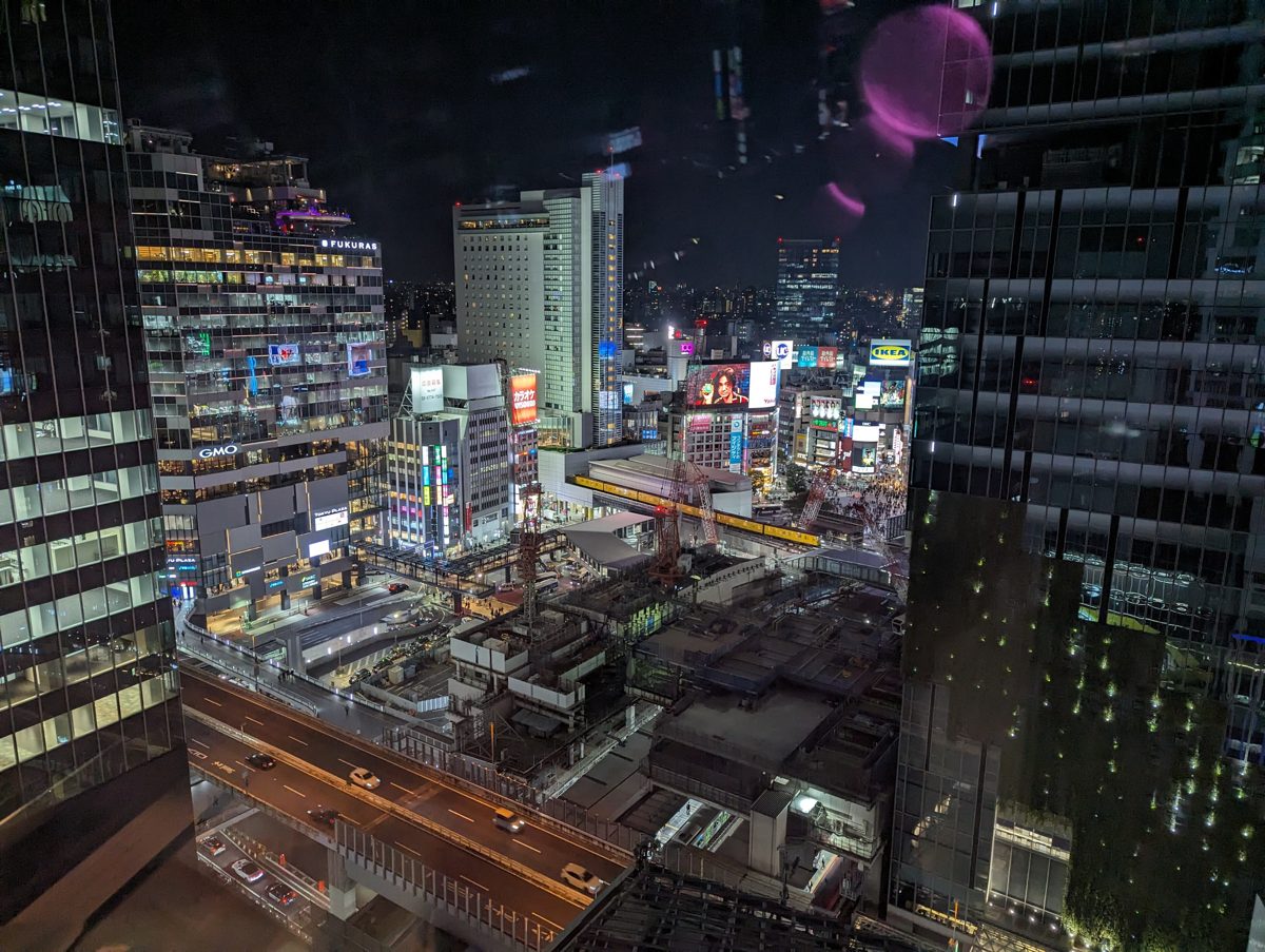 Night view over Shibuya from a high floor, with lit office towers, signs and an elevated road below