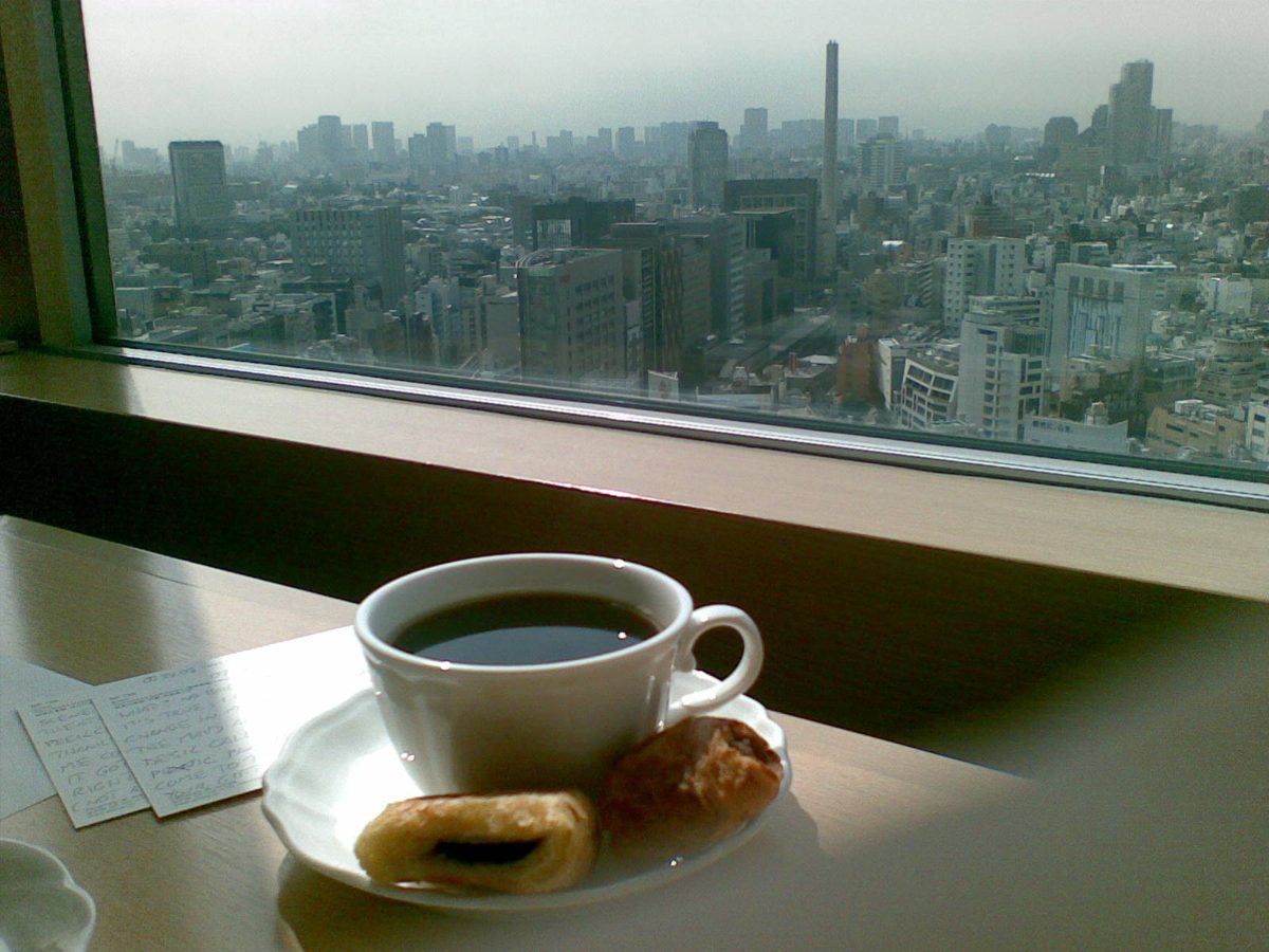 A cup of coffee and pastries on a window ledge looking out over a hazy Tokyo skyline
