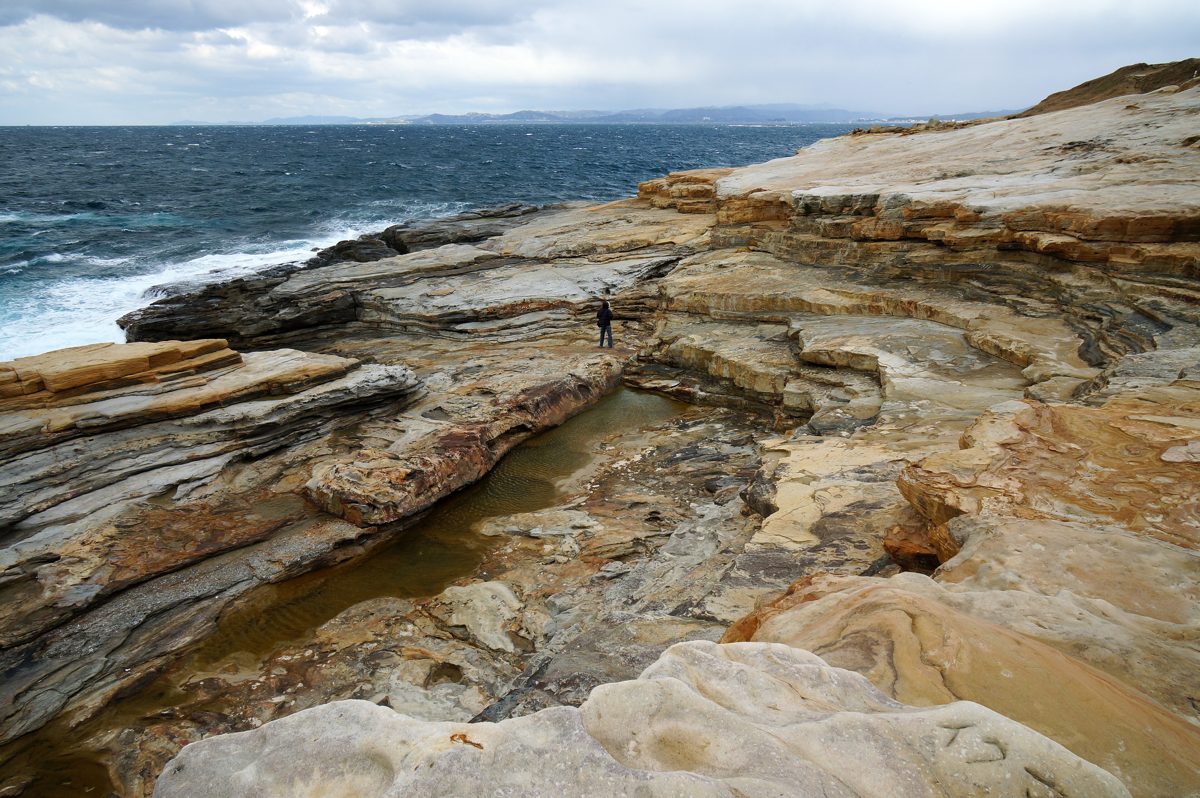 Layered sandstone rock shelf by the sea under a cloudy sky