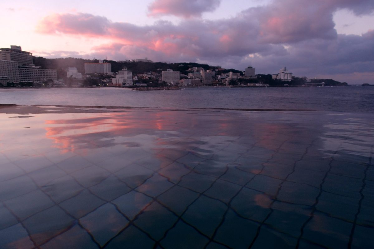 Wet paving reflecting a pink sunset sky over a bay lined with buildings