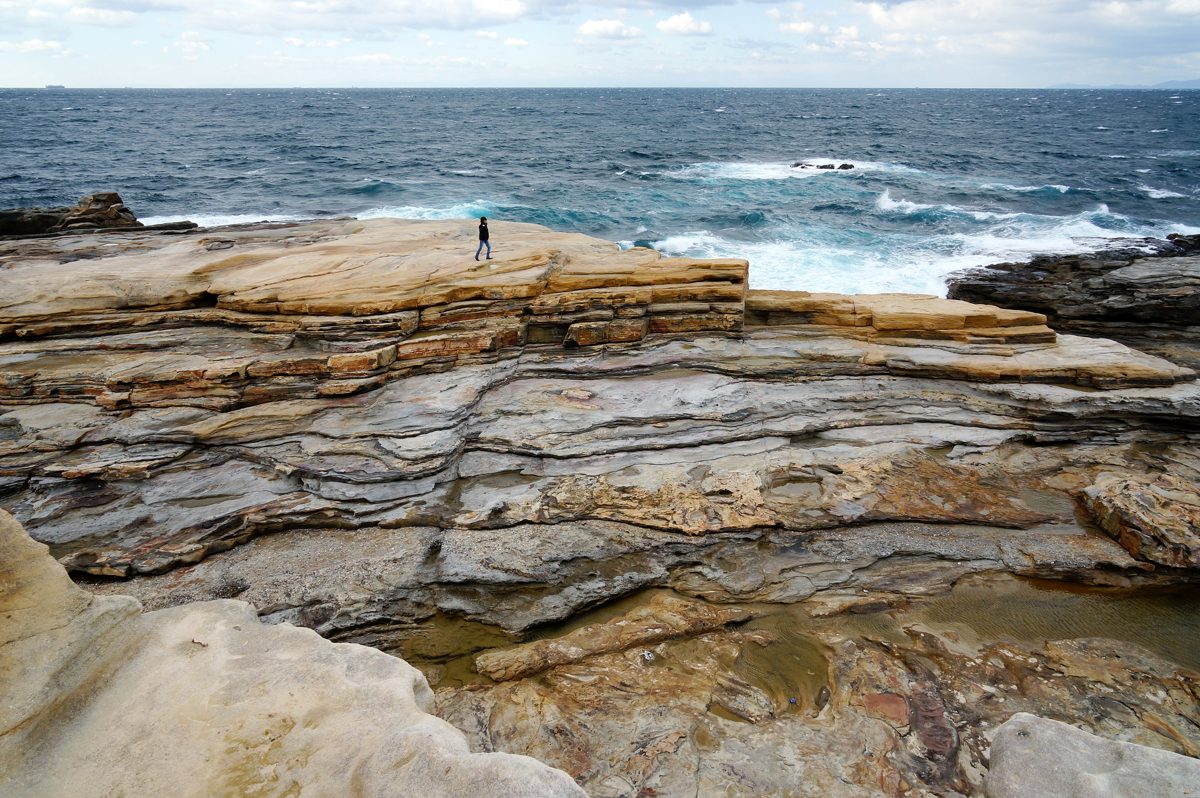 Wide, layered sandstone rock shelves running out to the sea under a pale sky