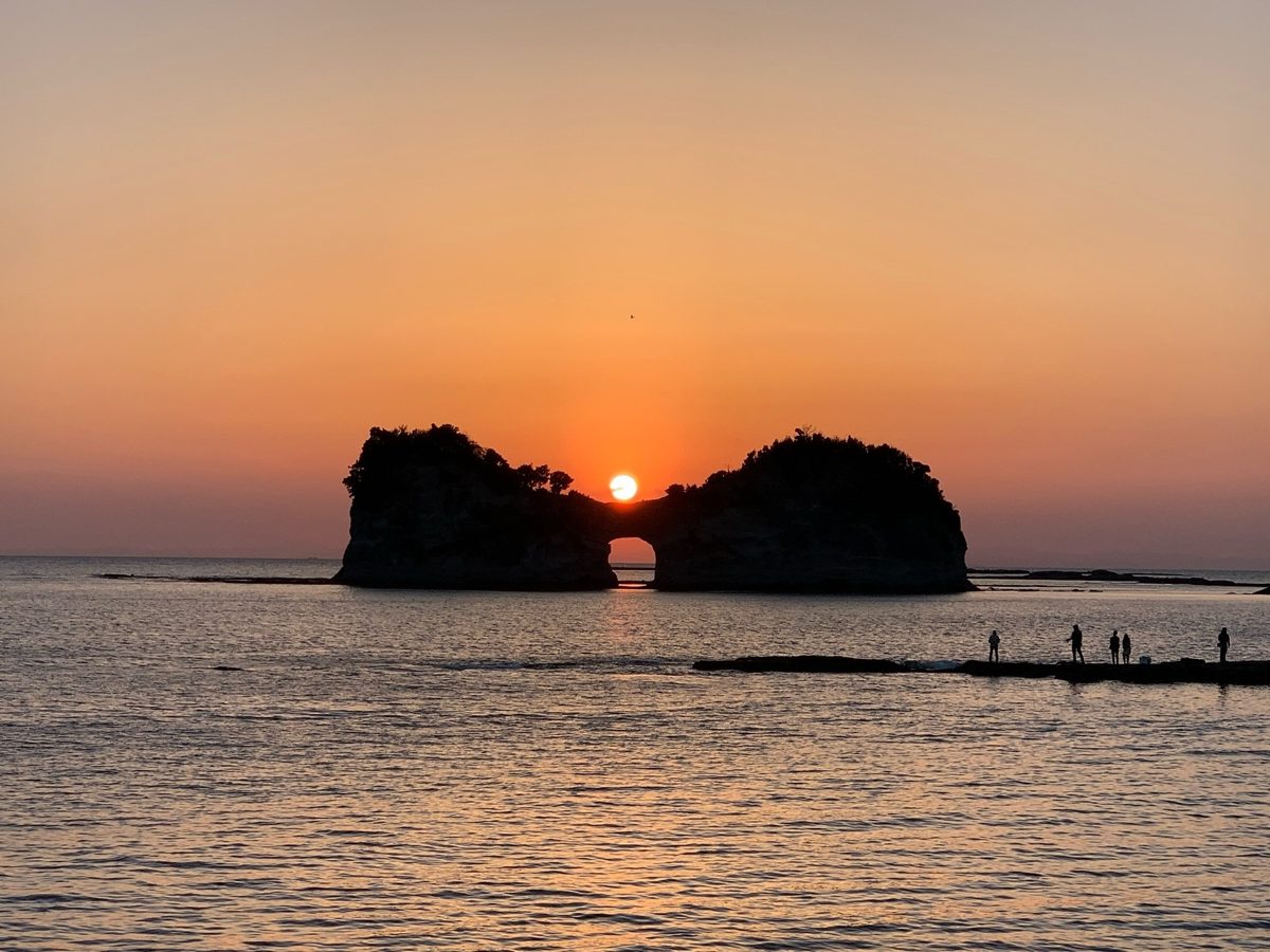 The sun setting through the arch of Engetsu Island, with the sea in orange light