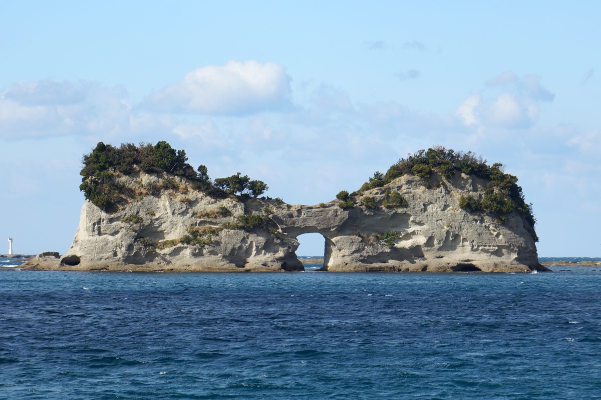 A rocky islet with trees on top and a round arch through its middle, in a blue sea