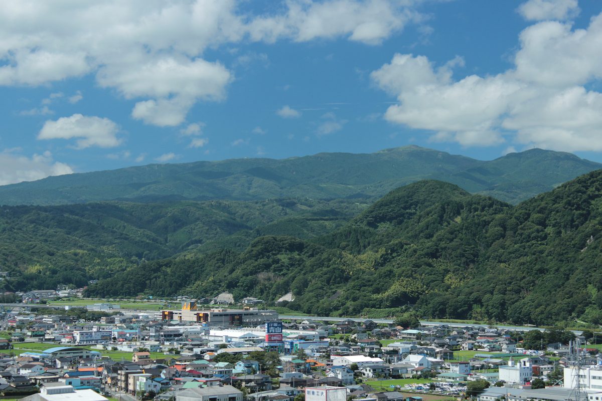 Green volcanic mountains of the Daruma volcano under a blue sky, with a town in the valley below