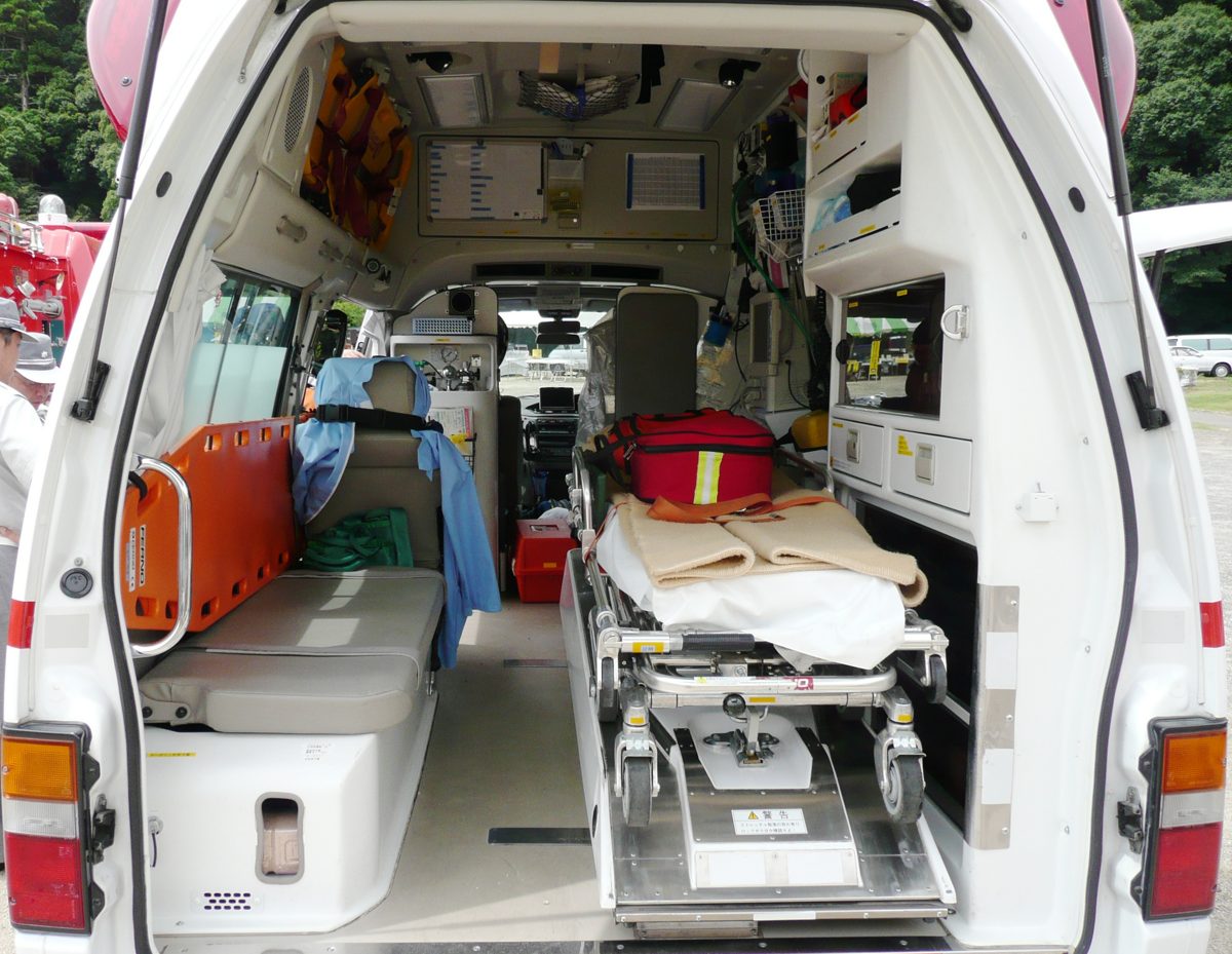 The open back of an ambulance showing a stretcher, a red medical bag, and equipment shelves