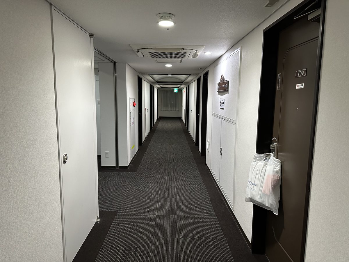 A long carpeted guest-floor corridor with room doors in a Japanese business hotel