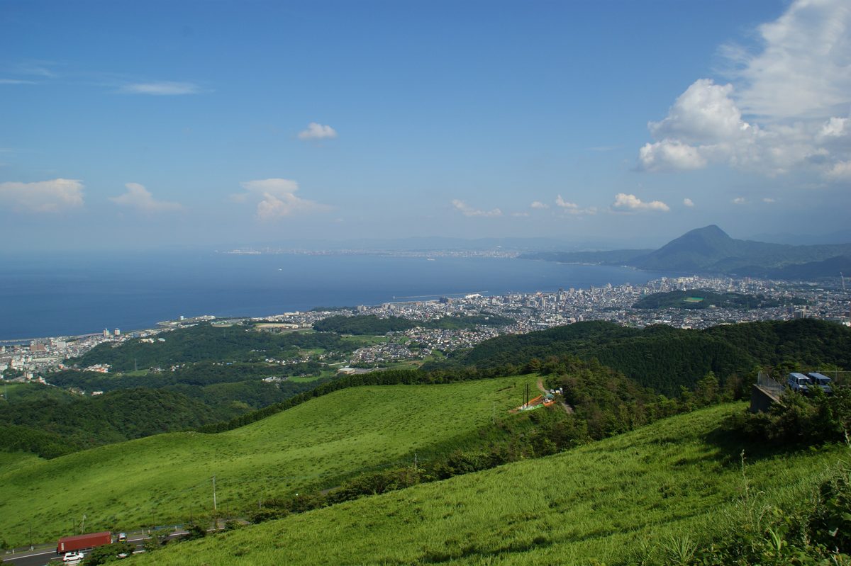 Green hillsides sloping down to a coastal city and a wide blue bay