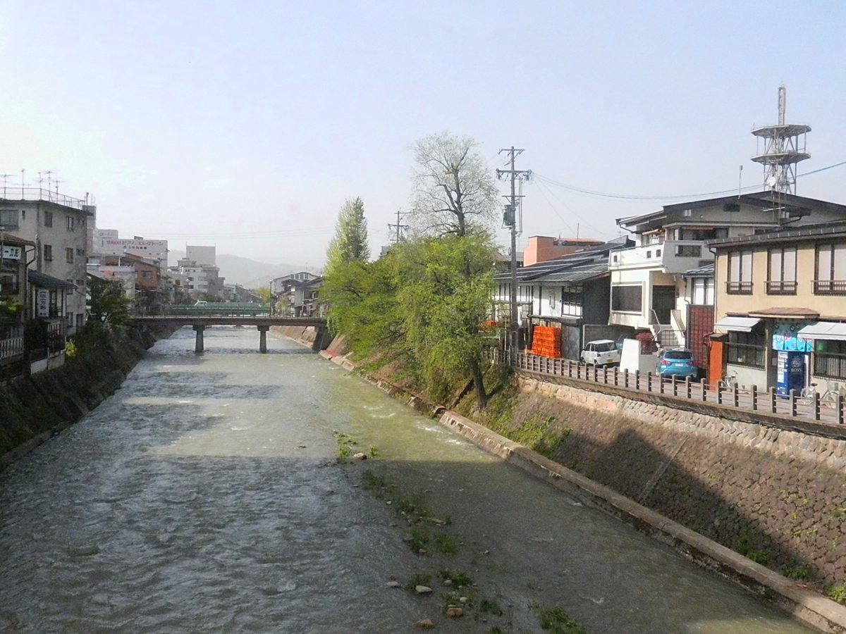 The Miyagawa River flowing between stone embankments and houses, with a bridge in the distance