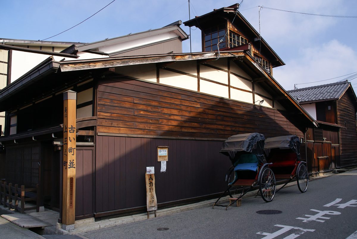 Two rickshaws parked beside dark wooden buildings on a street in old Takayama