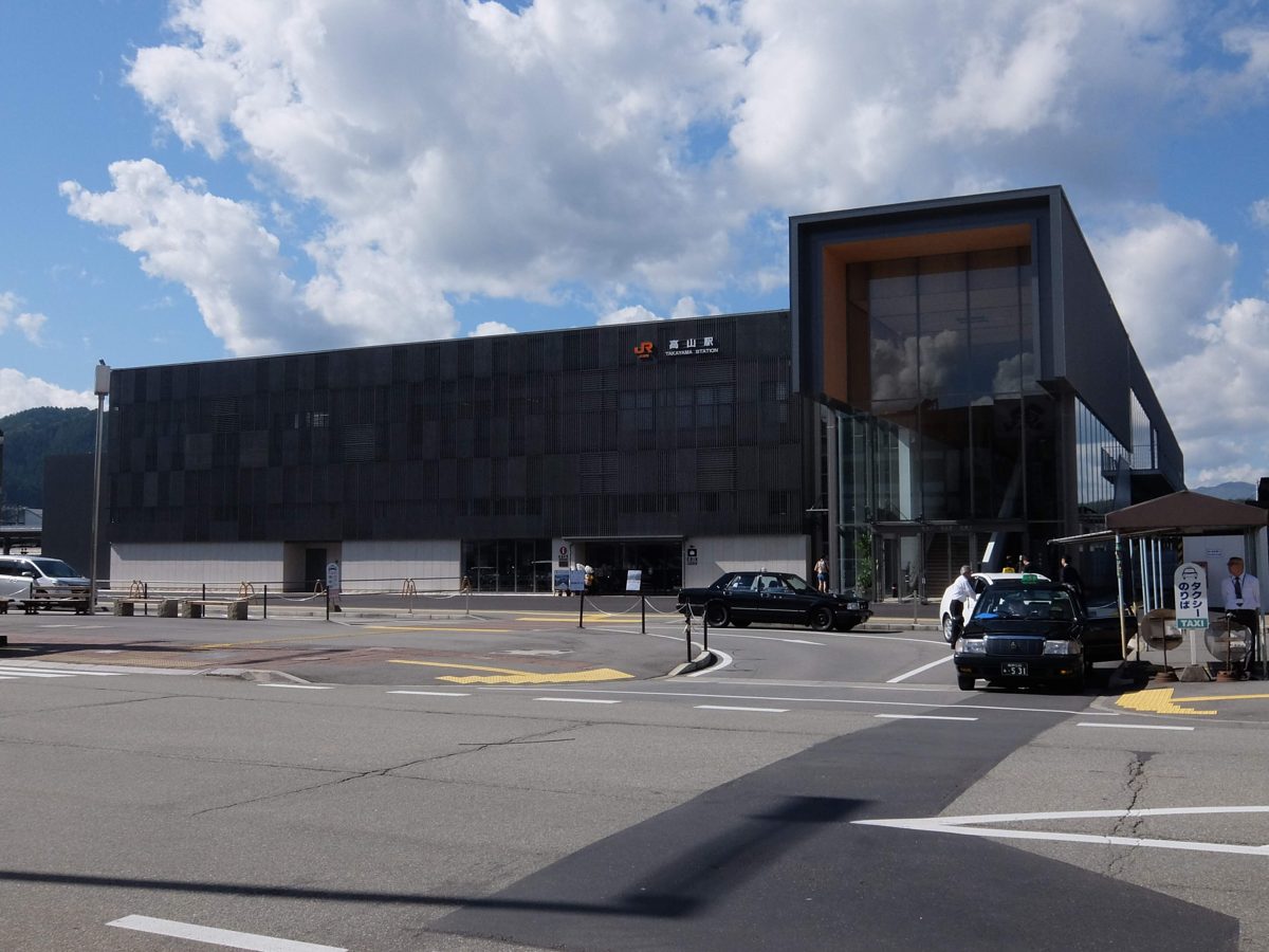 A modern dark station building with a wood-framed glass entrance under a blue sky