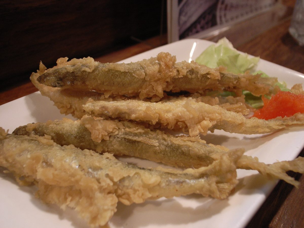 Several pieces of whole small fish tempura on a white plate
