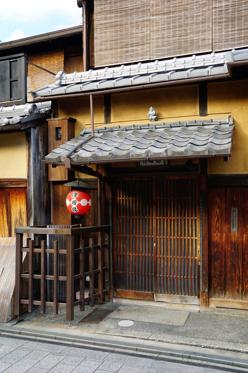 Entrance of a traditional wooden townhouse with a hanging lantern and lattice windows in Gion, Kyoto