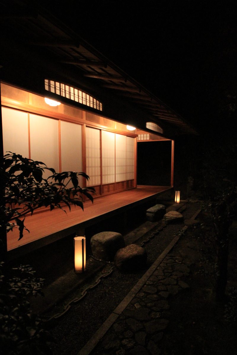 A lit wooden building beside a garden path with stone lanterns at night