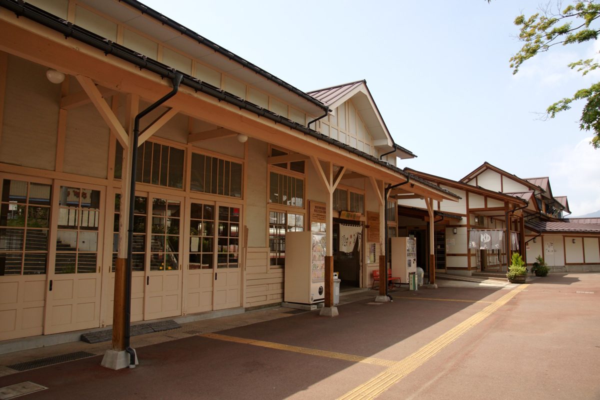The wooden front of Yudanaka Station on a sunny day, with long eaves and an empty forecourt