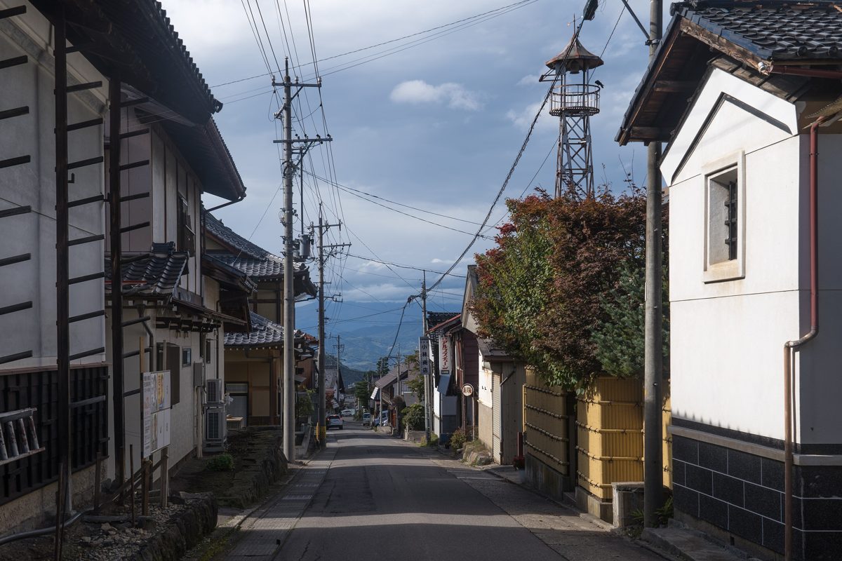 A quiet street with old tiled-roof houses, white storehouse walls and an old fire lookout tower, with mountains in the distance