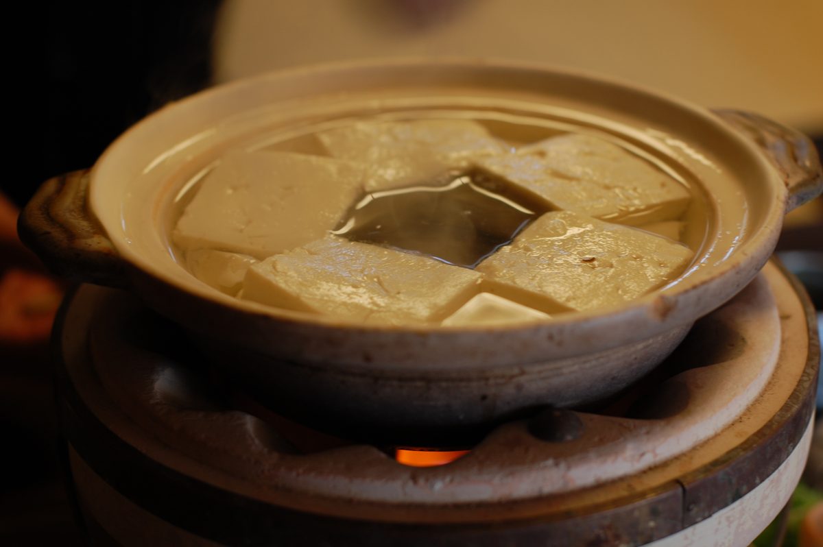 Blocks of tofu simmering in a clay pot over a small flame