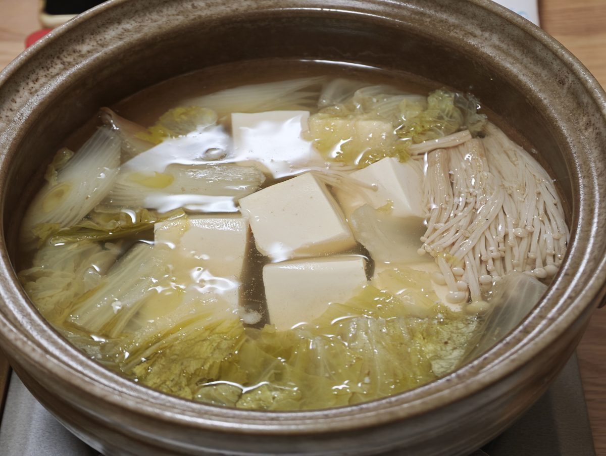 A clay pot of yudofu with tofu cubes, napa cabbage and enoki mushrooms