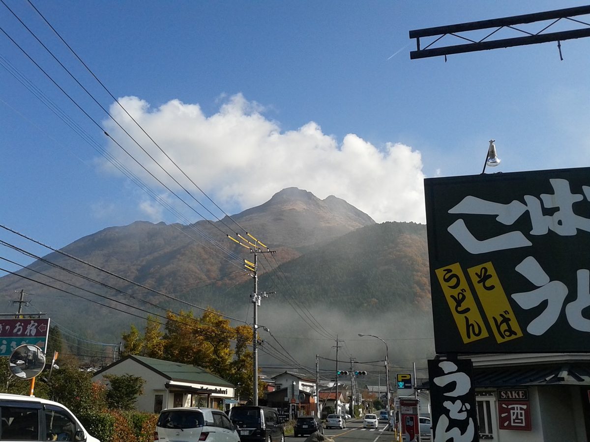 A street in Yufuin with shop signs and Mount Yufu behind it