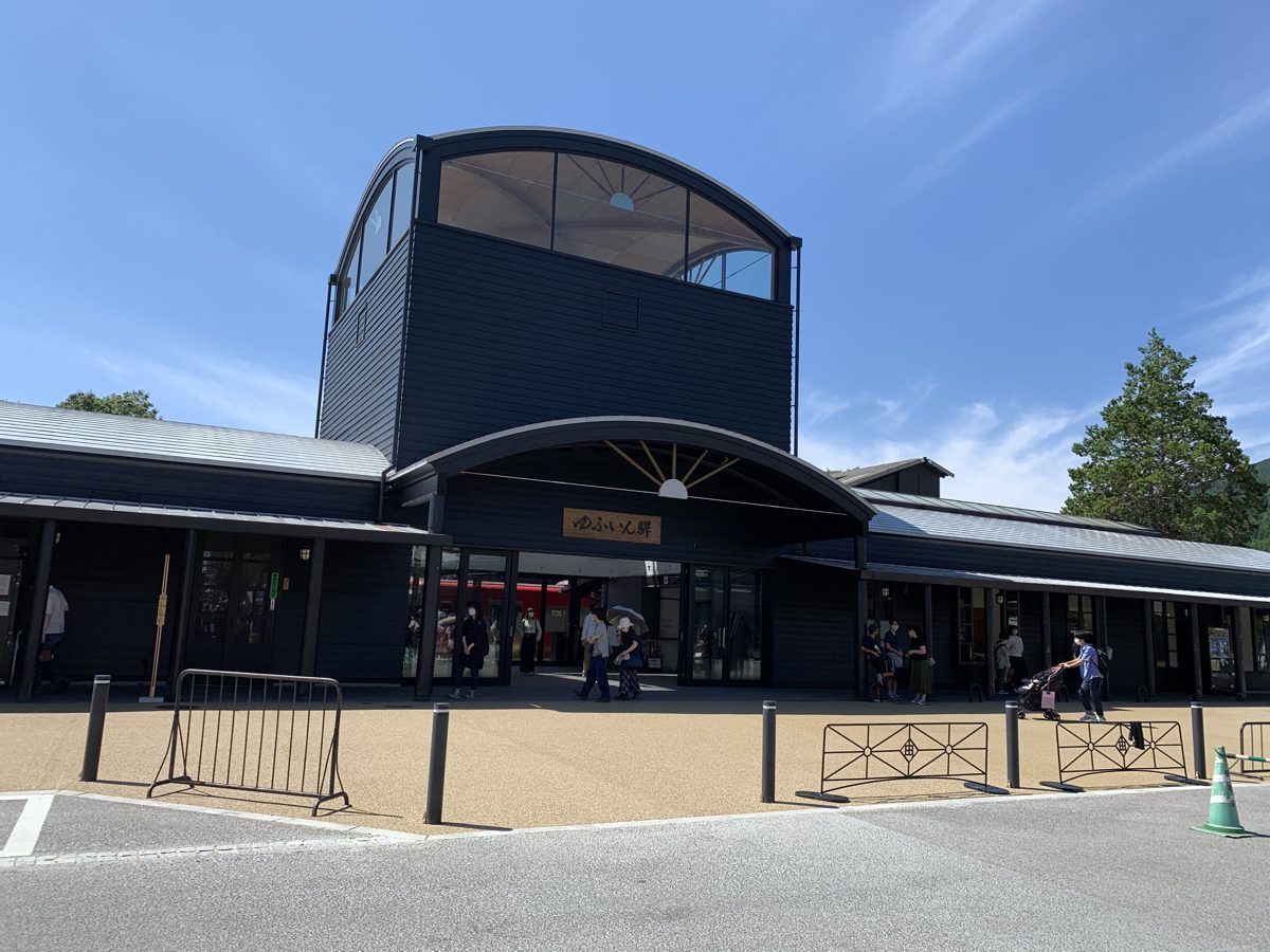 The dark wooden building of JR Yufuin Station with its arched roof under a blue sky