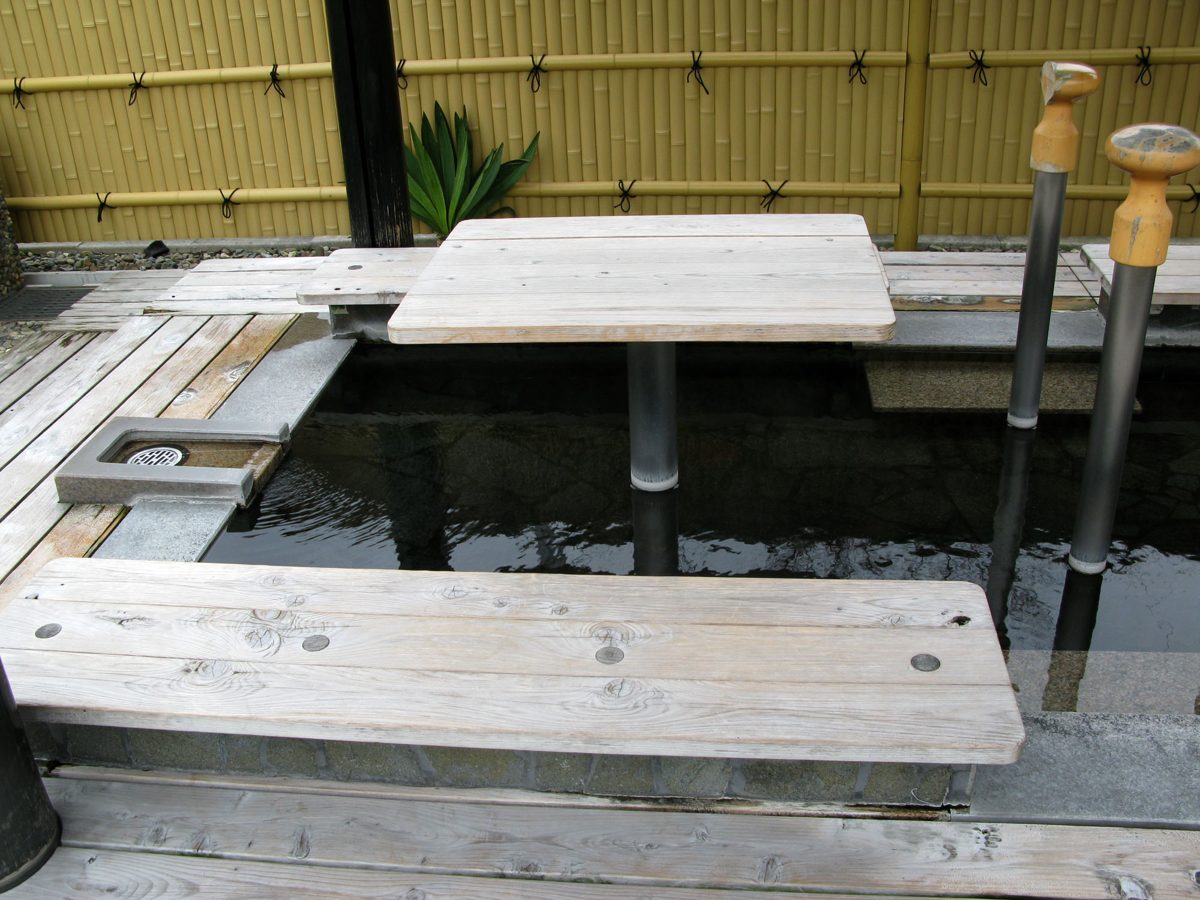 A wooden foot bath with benches and a bamboo fence at Yufuin Station