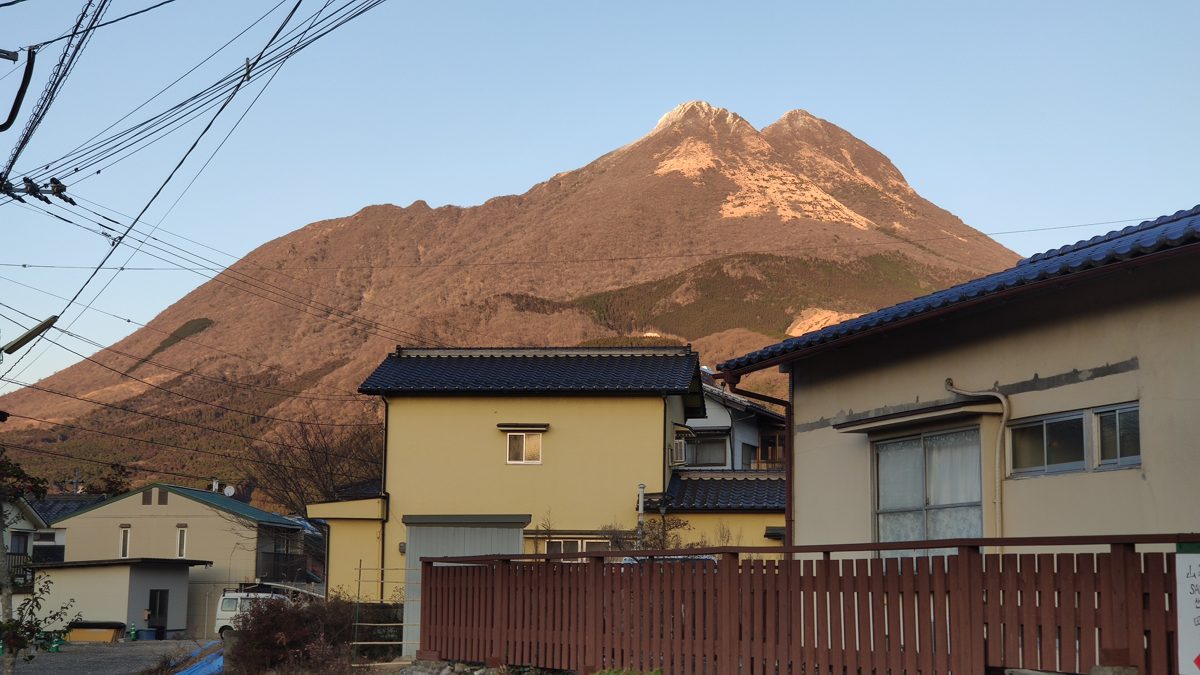 Mount Yufu rising behind low houses in Yufuin under a clear blue sky
