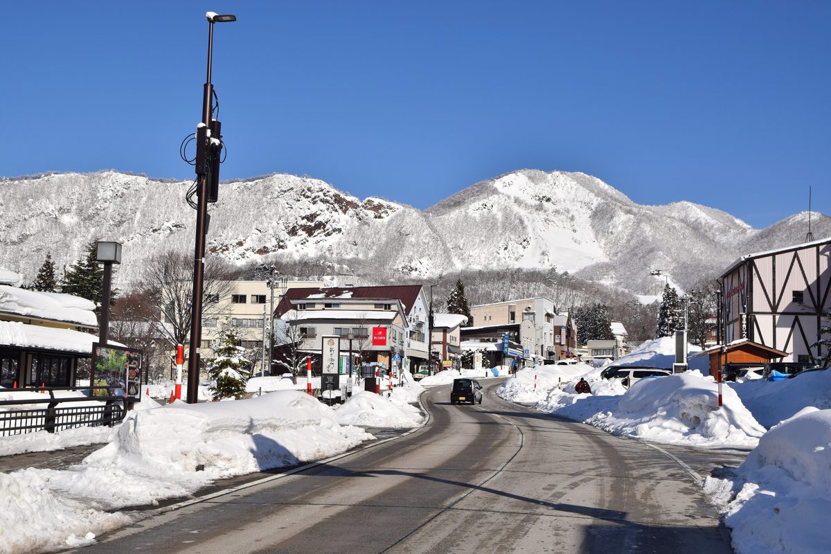 A snowy street in Zao Onsen village with snow-covered mountains under a blue sky