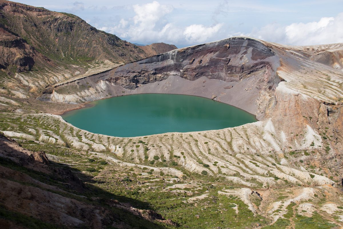 A green crater lake surrounded by bare volcanic slopes