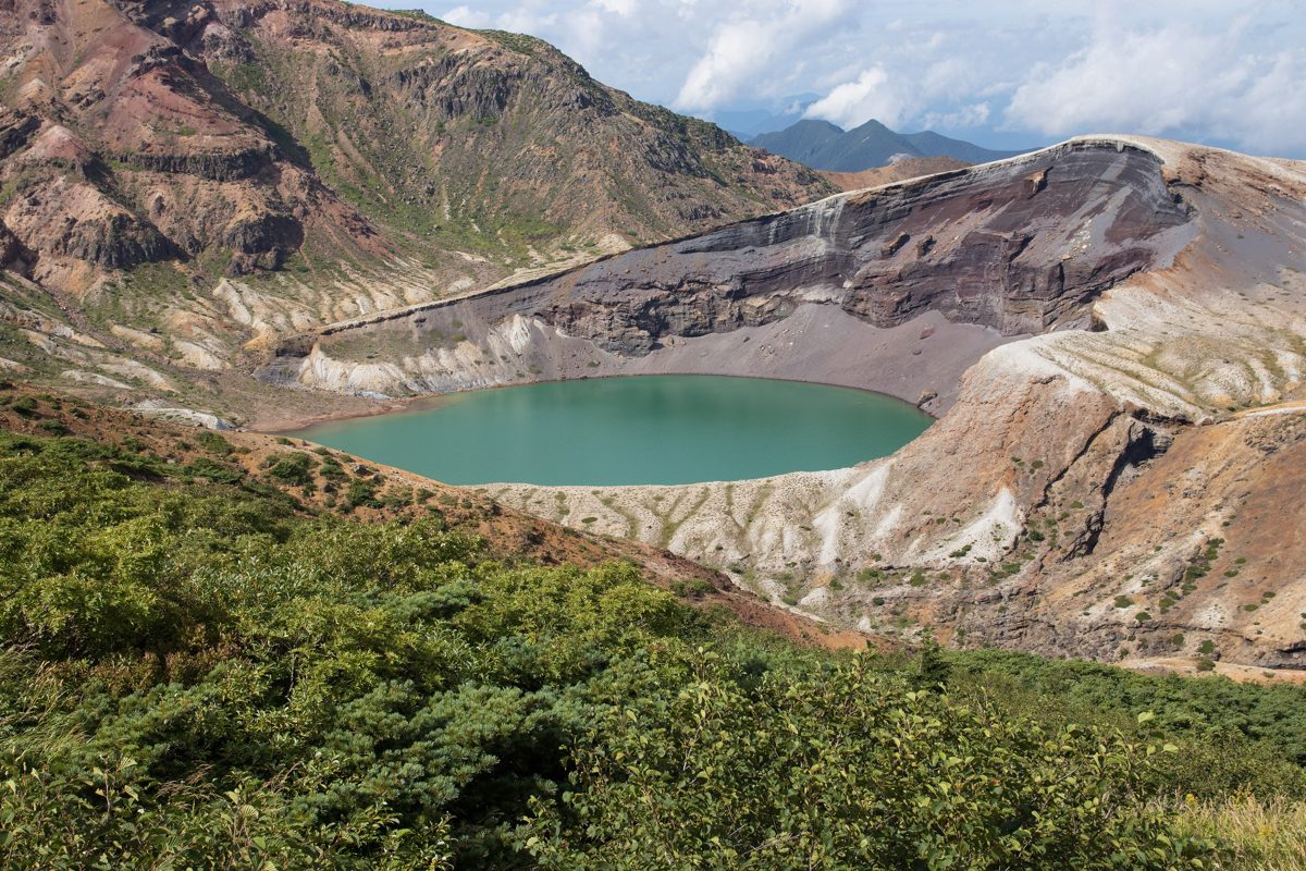 A green crater lake surrounded by bare volcanic slopes under a blue sky